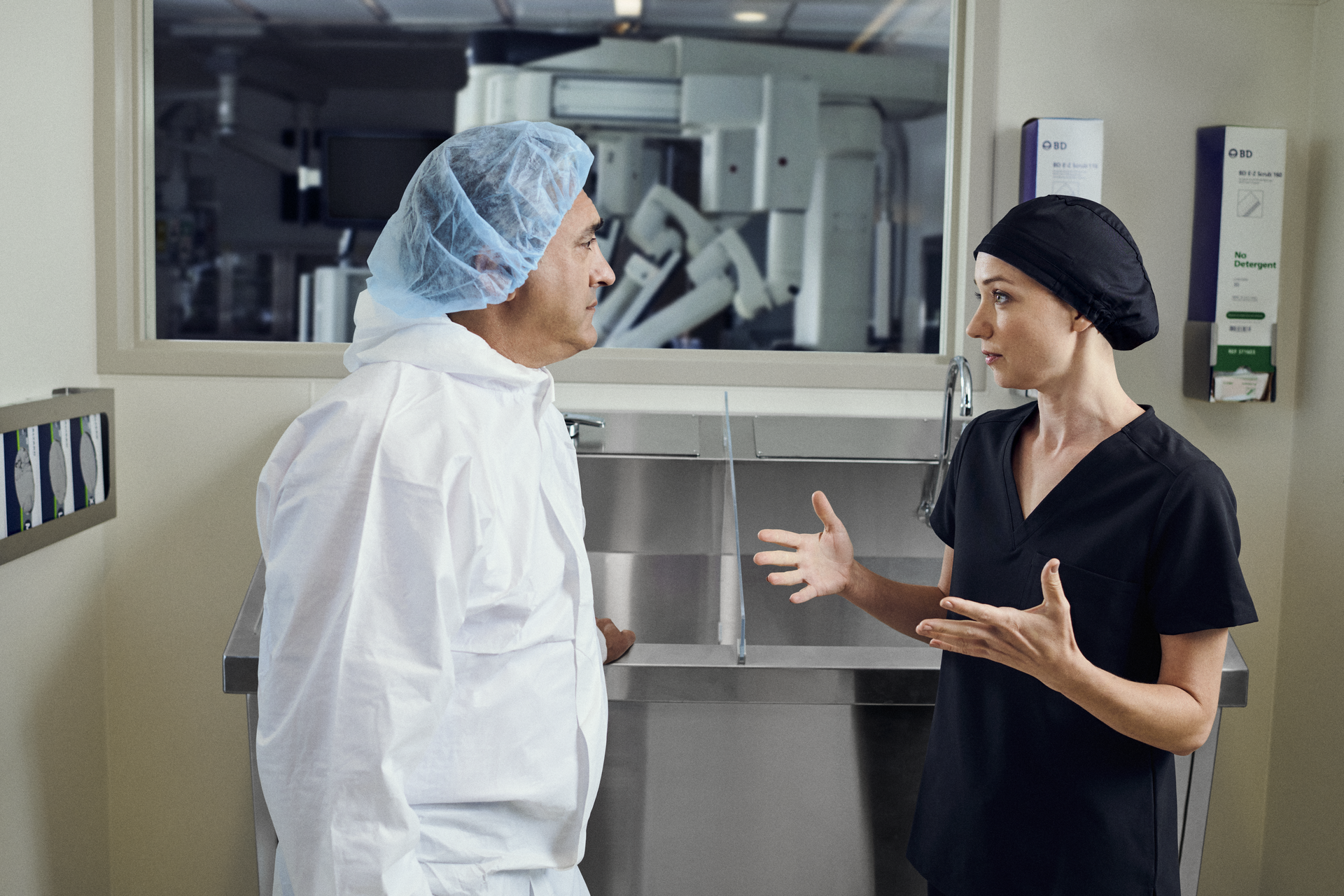 Executive at scrub sink with surgeon and da Vinci in background