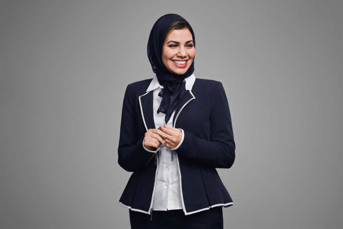 A smiling woman in a headscarf and jacket on gray