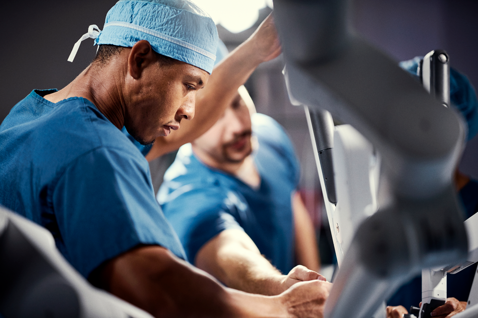 A care team member helps a surgeon perform surgery with a da Vinci system.