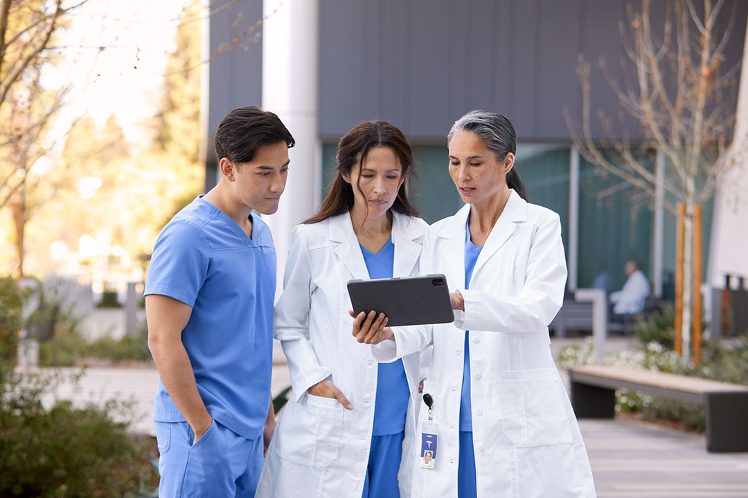 Three surgeons outside a hospital viewing a tablet