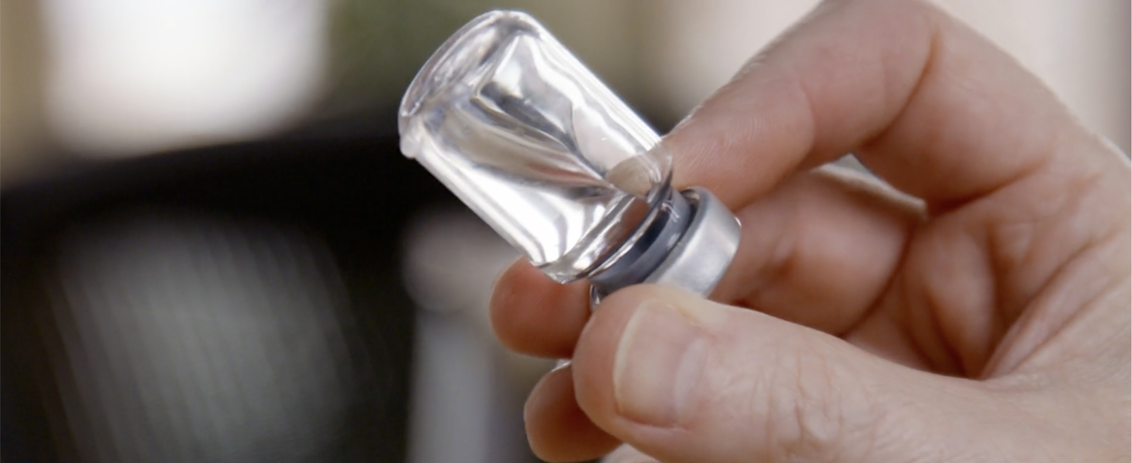 A hand holds a vile with a clear liquid in it